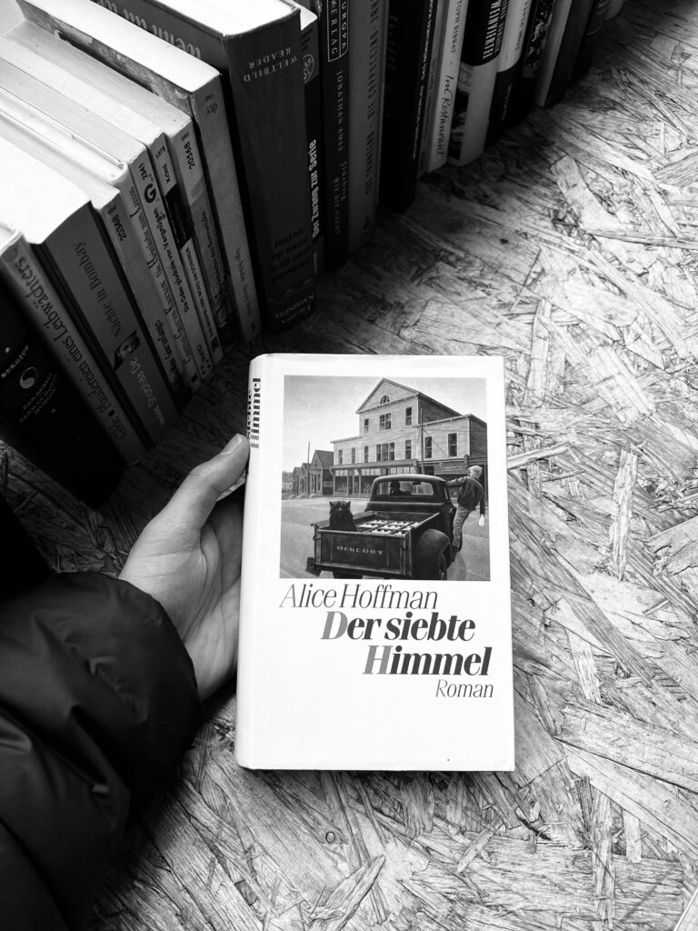 A person holds a book titled 'Der siebte Himmel' by Alice Hoffman in a bookstore.