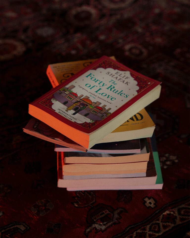 A vertical stack of books lying on a patterned rug, suitable for literary-themed content.